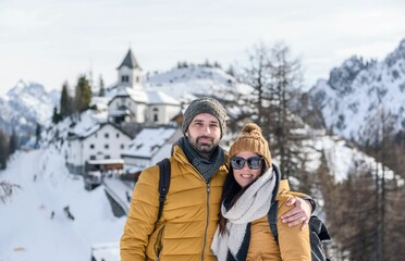 Fototapeta premium Couple in front of mountaintop village of Monte Lussari in Julian alps, Italy