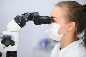 Female dentist using dental microscope treating patient teeth at dental clinic office