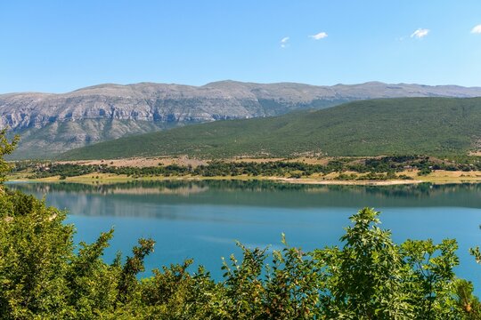 Lake Peruca in Croatia surrounded by trees, hills and Dinara mountain range on a sunny day