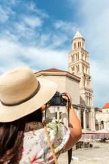 Deurstickers Woman in a sun hat holding up camera taking picture of a cathedral in Split, Croatia © Marko Klarić/Wirestock Creators