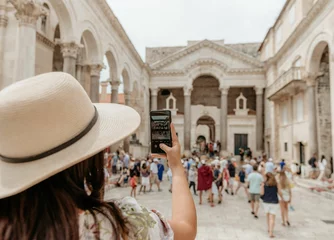 Deurstickers Rear view of woman taking a photo in a busy city square at Diocletian's palace in Split, Croatia © Marko Klarić/Wirestock Creators