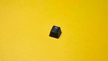 Black ''escape'' keyboard key isolated on yellow background Top view. Copy space.