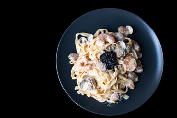 Delicious spaghetti with seafood:prawns, black caviar and sauce parmesan on black plate on black...