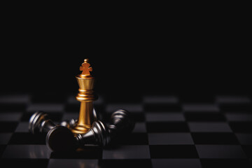 Gold king chess standing in center surround by fallen silver king chess, knight and other pieces in black background. Winner in business competition, marketing strategies and leadership concept. © TimmyTimTim