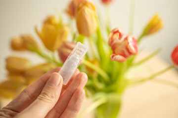 medicine in a plastic container in the hands of a girl against the background of tulips. Spring transformation, serum for care, beauty. Plastic recycling, use, consumption