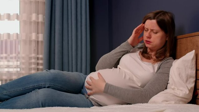 A pregnant woman in bed feels a headache and tries to calm her baby by stroking the belly. How to get rid of headaches when you are pregnant.