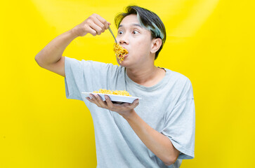 asian man in a grey tshirt eating noodles using fork hungrily
