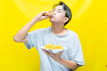 Happy euphoric asian young man in grey tshirt eating instant fried noodle using bamboo chopstick...