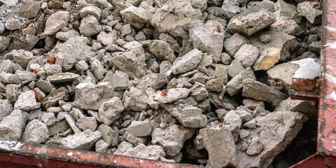 Construction concrete debris in metal dumpster close up. Cement scrap in container on construction site.