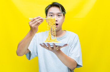 Happy euphoric asian young man in grey tshirt eating instant fried noodle using bamboo chopstick...