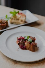 Vertical of two deserts on white plates on a wooden table against a dark, blurred background