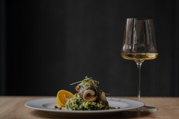 Closeup of a dish with fish on a plate and a glass of white wine on a wooden table