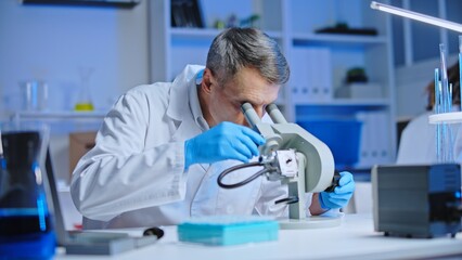 Laboratory technician examining virus cells under microscope, vaccine development