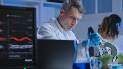 Plant breeding scientist working in laboratory, studying sample under microscope