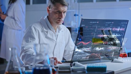 Serious male scientist studying graphs on holographic screen in experimental lab
