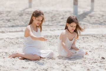 two happy little girls play on a white sandy beach near the ocean in summer. Children's holidays. Earth Day. Children's Day.Space for text