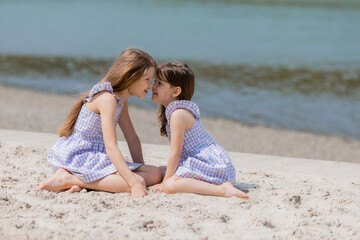 Fototapeta na wymiar happy little girls with long hair play on a sandy beach near the sea on a sunny day. Children's Day.Space for text