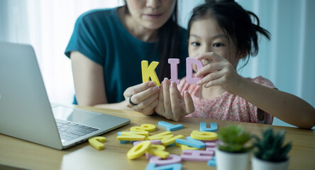 Happy mother and preschool daughter playing with set of colors letters.