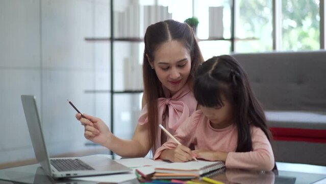 Asian woman teaching her daughter a homework.