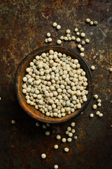 White peppercorns in a wooden bowl. Spices and condiments. Top view. On a rusty textured background.