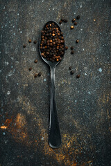 Fragrant black peppercorns in a metal spoon. Spices and condiments. Top view. On an old textured background.