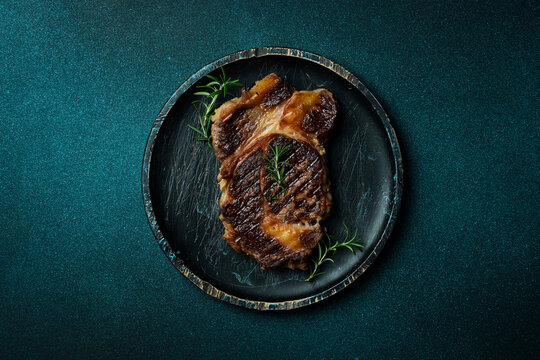 Grilled ribeye beef steak with spices on a wooden plate. On a dark blue stone background. Top view.