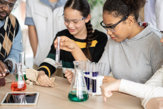 Diversity group of students in protective eyeglasses in science class doing chemical experiment in laboratory. Teacher watching girl mixing chemistry in test tube. learning and education concept