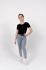 A young brunette girl of European appearance in a black T-shirt and blue jeans on a white background