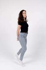 A young brunette girl of European appearance in a black T-shirt and blue jeans on a white background