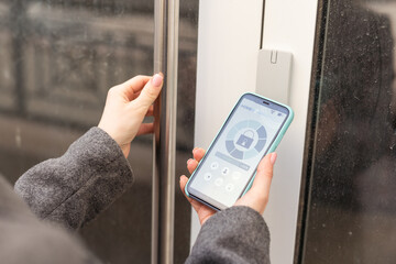 Woman locking smartlock on the entrance door using a smart phone. Concept of using smart electronic locks with keyless access.