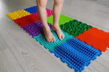 The child walks on an orthopedic massage mat for legs of different hardness and texture. Prevention of flat feet, hallux valgus in children, strengthening of the ankle joint