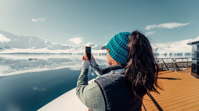 Female Tourist On Luxury Antarctica Cruise Ship Looking Out At The Stunning Scenic Arctic Landscape, As She Takes a Photo with her Phone, Landscape Shot