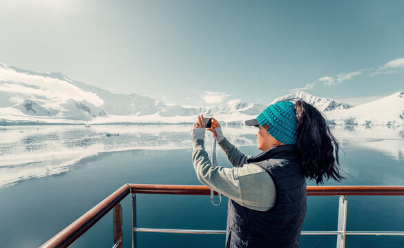 Female Tourist On Luxury Antarctica Cruise Ship Looking Out At The Stunning Scenic Arctic Landscape, As She Takes a Photo with her Phone off Top Deck