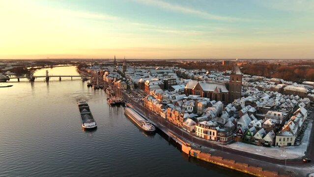 Kampen city view with ships at the river IJssel during a cold winter sunrise at the start of a cold bright winter day with light snow on the roofs. Kampen is an ancient Hanseatic League city at the sh