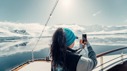 Female Tourist On Luxury Antarctica Cruise Ship Looking Out At The Stunning Scenic Arctic Landscape, As She Takes a Photo with her Phone off Top Deck over Bow of Ship