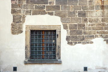 Square window with a metal grill against a partially plastered wall of stone blocks. From the Window of the World series.