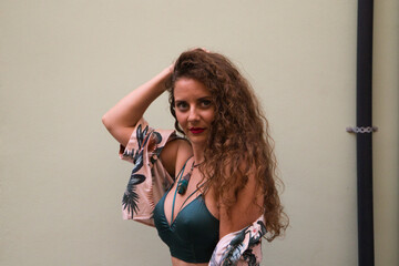 Beautiful woman, young and blonde with curly hair and blue eyes looks at the camera in a sexy way while touching her hair. In the background there is a beige wall. Concept different expressions.