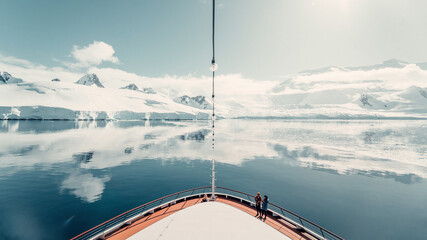 Snow Glacier Covered Mountains Reflecting in the Still Arctic Water of Antarctica, With Cruise Ship Bow in Shot © ANITEK MEDIA 