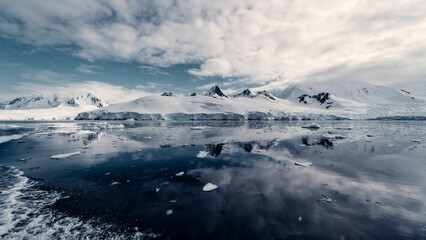 Fototapeta na wymiar Moody Landscape of Snow Glacier Covered Mountains Reflecting in the Still Arctic Water of Antarctica