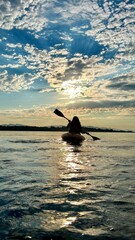 a teenage girl is kayaking at sunset in Pacific Ocean, only the silhouette of Kayak and Paddles is visible she swims along a sunny path to the sea. a beautiful sky with small clouds 08.2022 Canada 