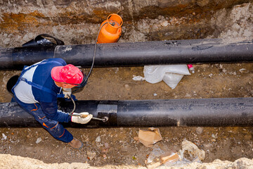 Worker is placing sheet of thermal insulation on new pipeline in trench