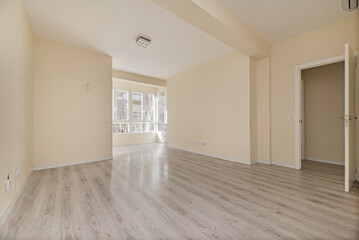 Obraz premium Empty living room with light laminated floors, a bay window with white aluminum and glass windows and walls painted in a smooth cream color
