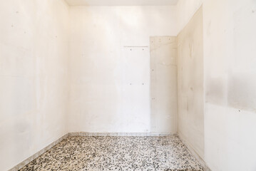 Empty living room with black dotted terrazzo floor and poorly painted walls in a plain white color
