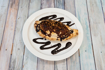 An empanada dessert with crushed nuts with a lot of chocolate syrup