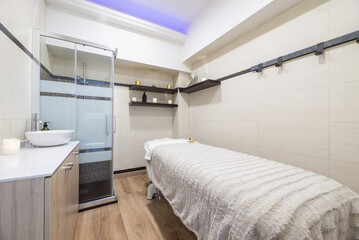 Fototapeta na wymiar Cabin of a clinic for aesthetic treatments with a massage table and a shower cabin with glass partitions