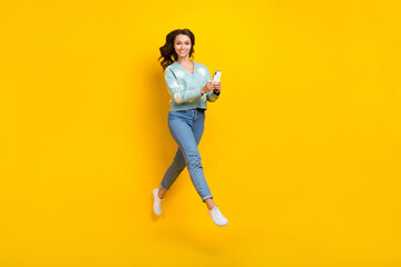 Fototapeta na wymiar Full length photo of sweet cute woman wear turquoise cardigan jumping high texting device isolated yellow color background