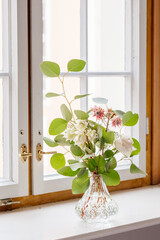 hübscher, wilder Blumenstrauß in Glasvase auf Fensterbrett vor Fenster
