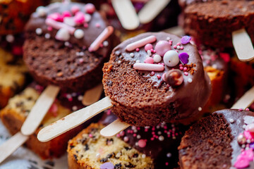 Cakesicles runde Kuchen am Stil mit Schokoladenteig und rosa lila Streuseln als dekoration in einer Nahaufnahme passend für Rezepte zum selber backen