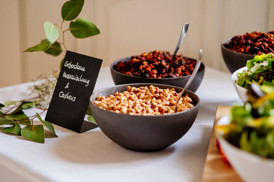 Cashews in einer sch&ouml;nen Keramiksch&uuml;ssel bei vegetarischem Buffet auf einer Feier im Hintergrund ein Schild mit der Beschriftung "Gebackene Nussmischung und Cashews"