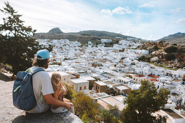 Family father and child traveling in Rhodes island, Greece sightseeing Lindos city white houses aerial view summer vacations lifestyle Europe destinations - obrazy, fototapety, plakaty